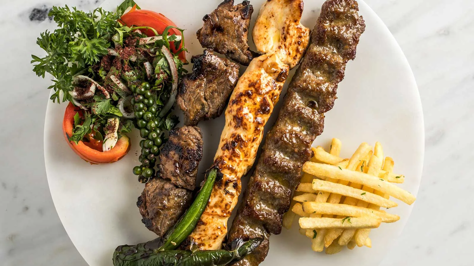 Mixed Persian grill platter with kebabs, salad and fries on marble