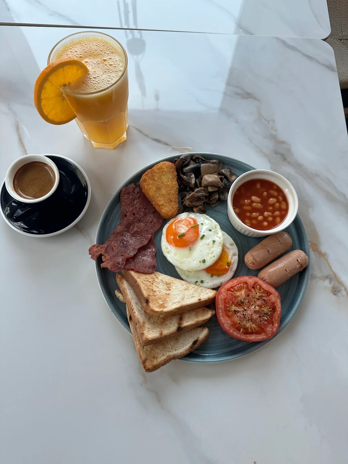 All-day breakfast plate with eggs, toast, grilled tomato and sausages, juice and coffee