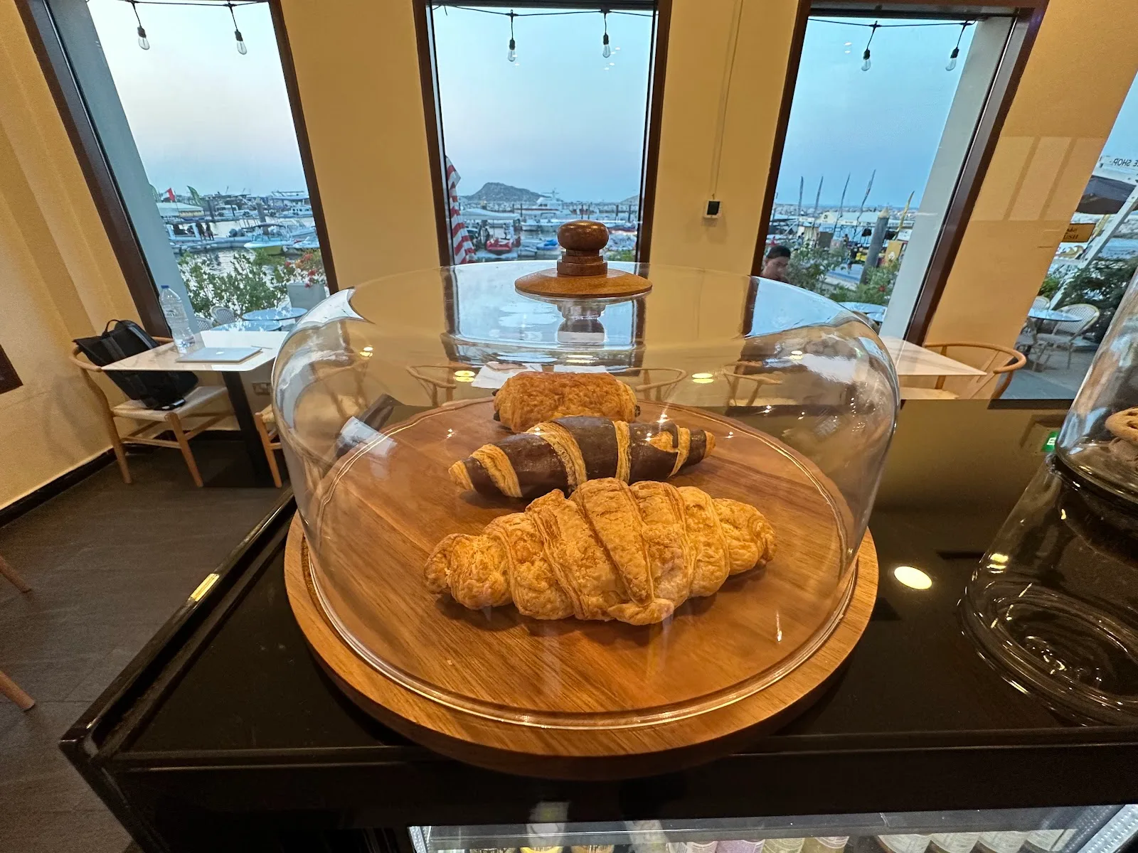 Croissants and pastries under a glass dome with the marina in the background