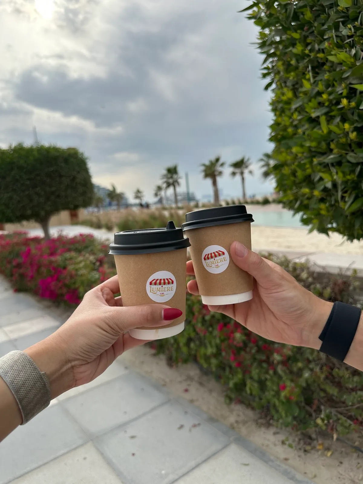 Two Lumière Coffee branded takeaway cups held up by the waterfront promenade
