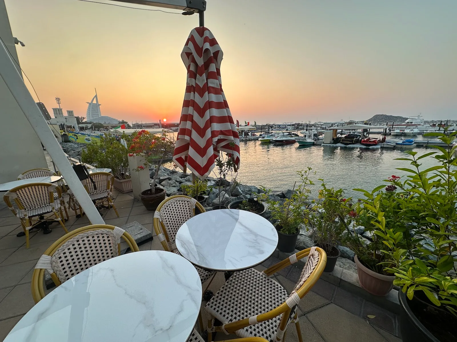 Sunset over the marina from Lumière Coffee's waterfront terrace, with a red-and-white striped umbrella and the Burj Al Arab on the horizon