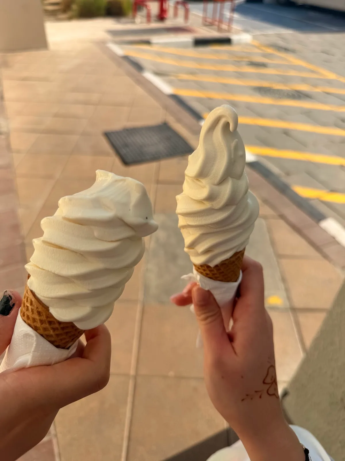 Two soft-serve ice cream cones held up in the sun