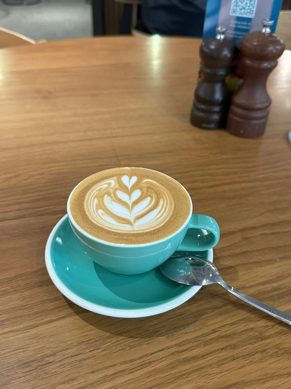 Latte with leaf latte art in a teal cup on a wooden table