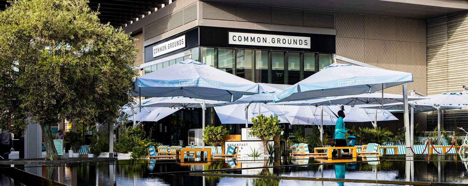 Outdoor terrace with pale-blue Common Grounds umbrellas beside a reflecting pool