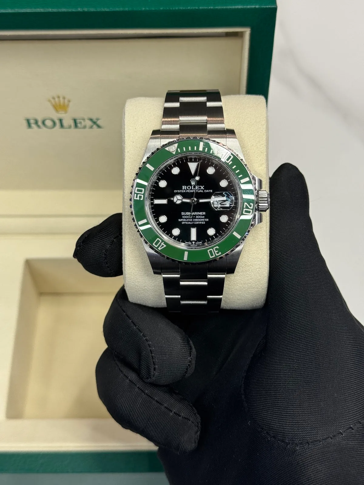 Gloved hand presenting a green Rolex Submariner with its box