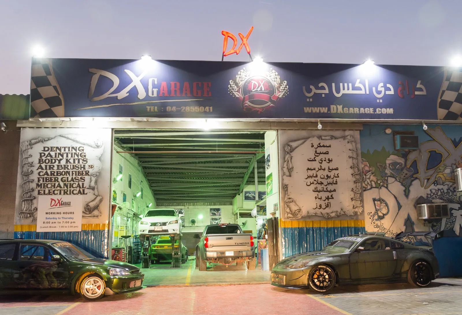 DX Garage workshop in Al Quoz lit up at night, with cars parked outside and the service list painted on the wall