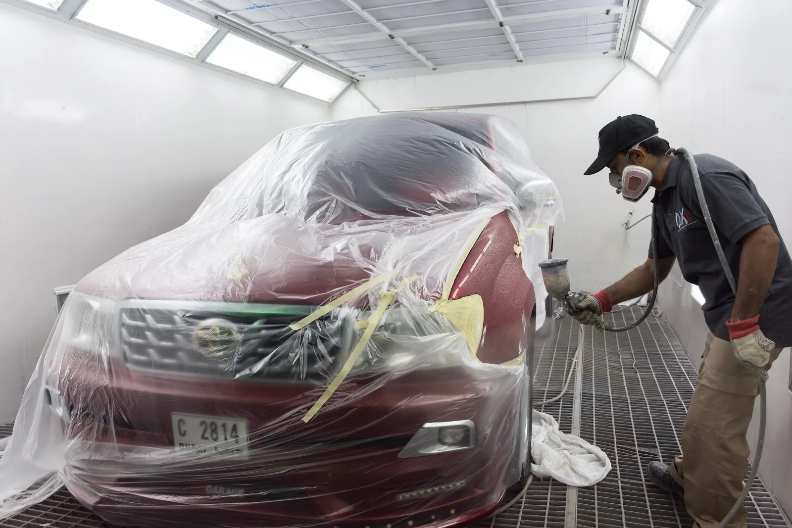 DX Garage technician spray-painting a car inside the refinish booth