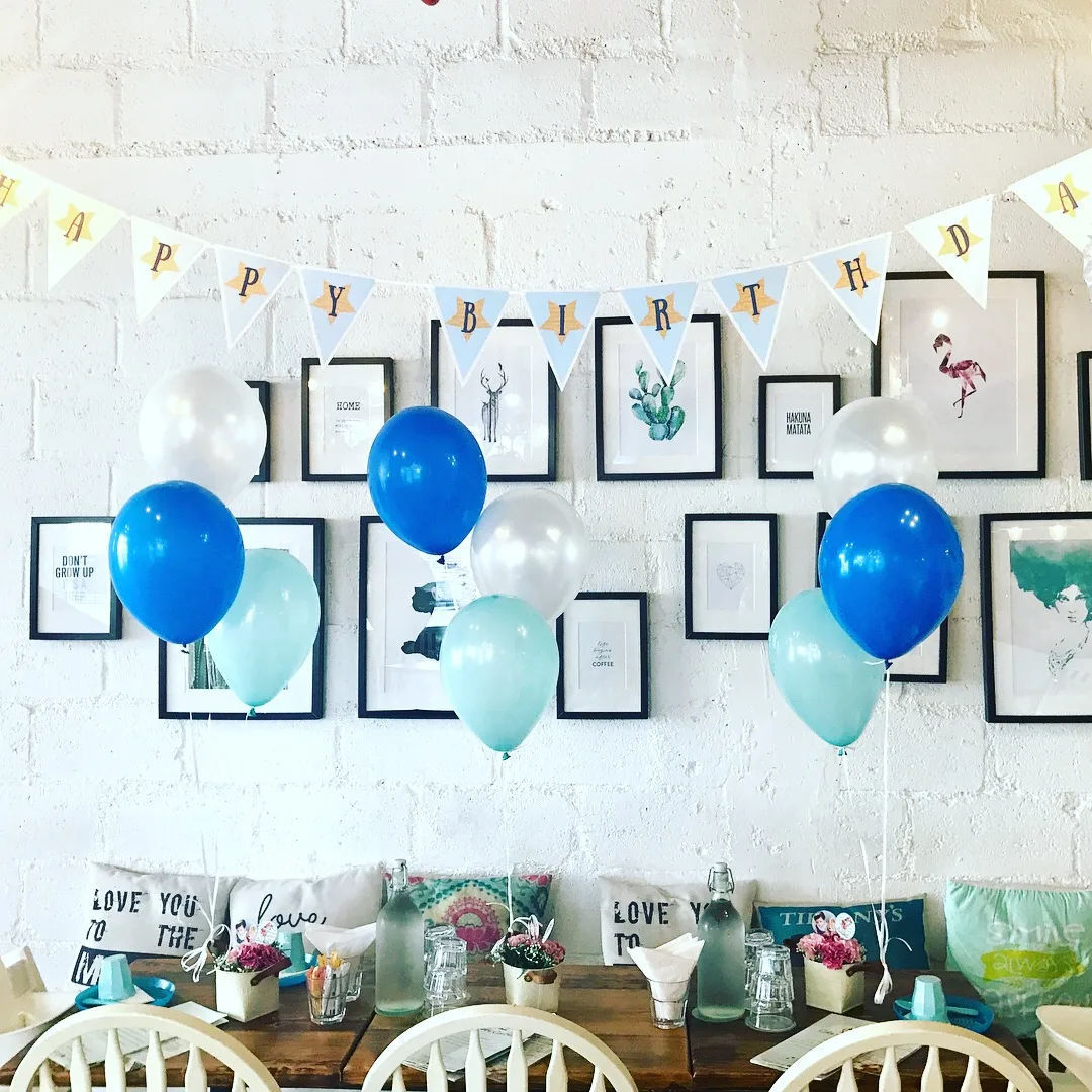 A birthday table set up with balloons and a happy birthday banner on the gallery wall