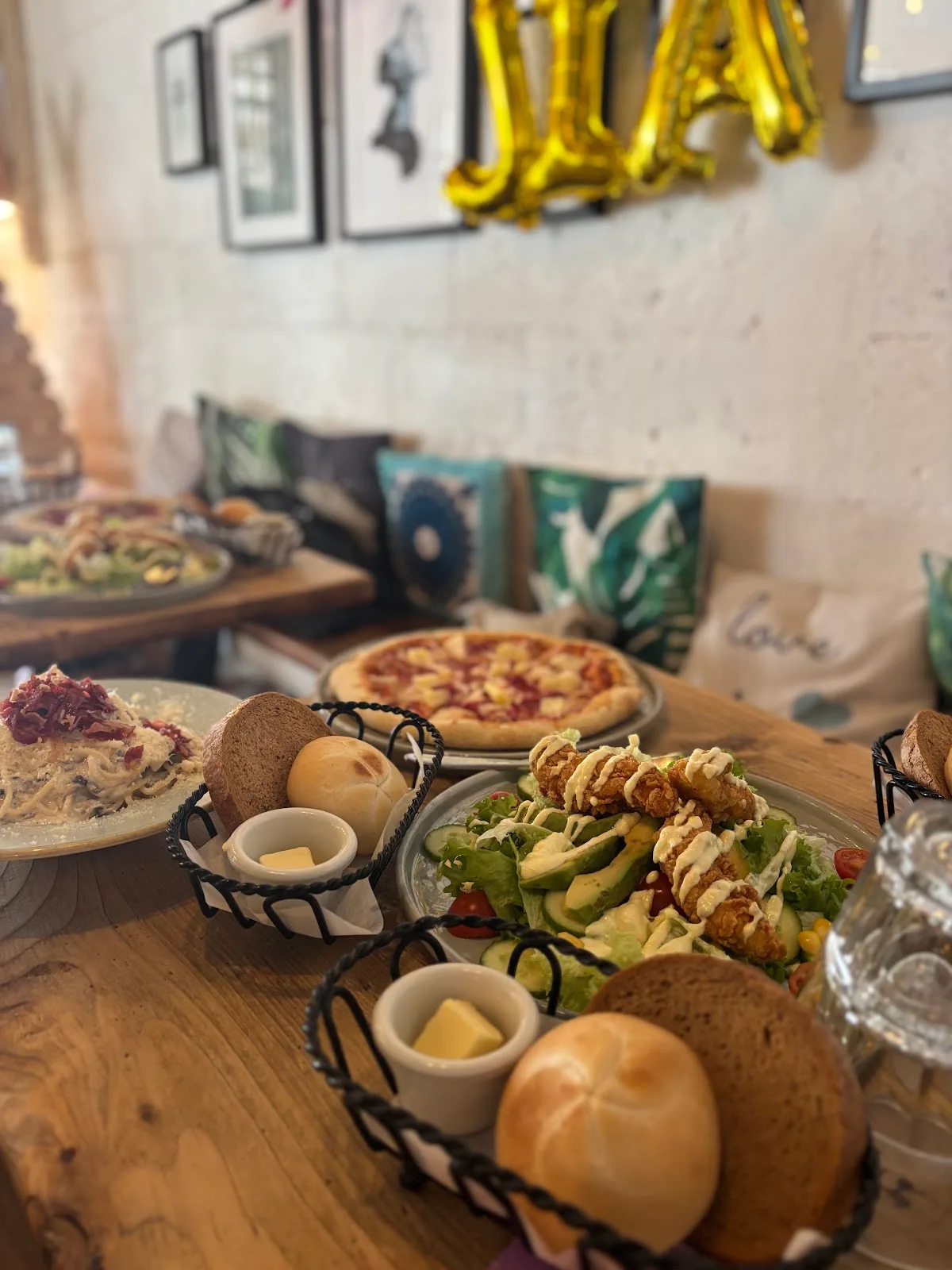 A spread of pizza, salad and pasta with bread baskets on a wooden table