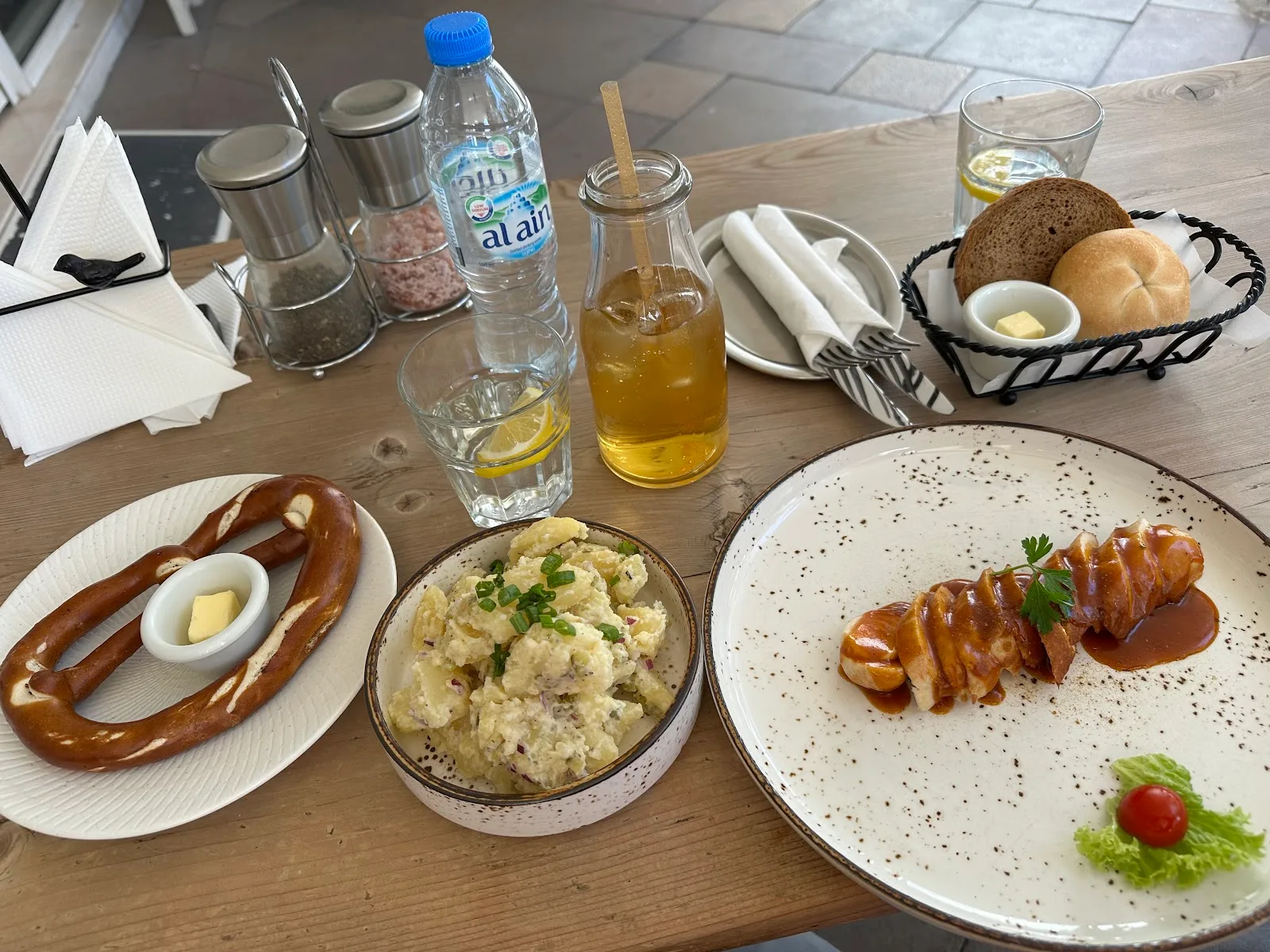Soft pretzel with butter, potato salad and sausage in gravy on speckled plates