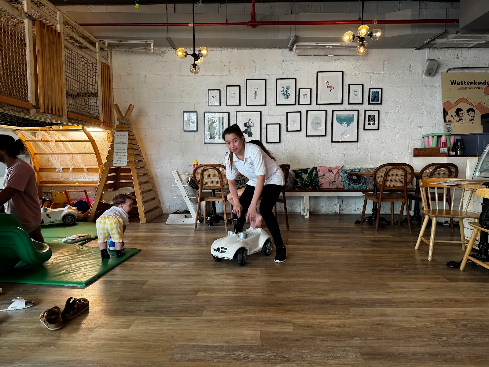An adult playing with a toddler and a ride-on car in the café's play space