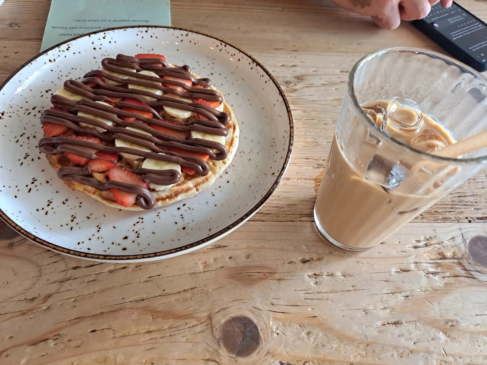 Waffle topped with strawberries, banana and chocolate sauce beside an iced coffee