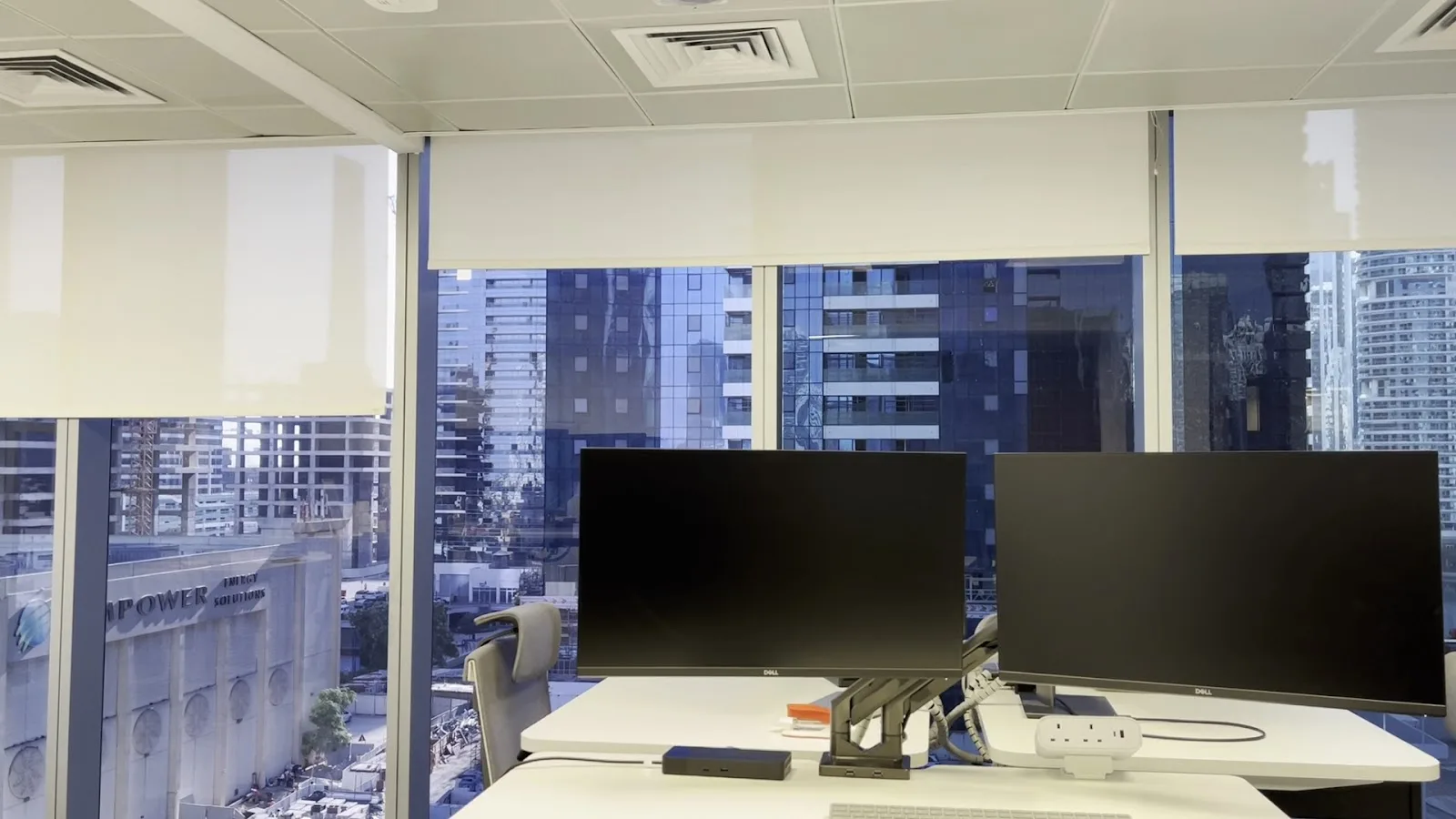 Office with roller blinds over floor-to-ceiling glazing and a city view