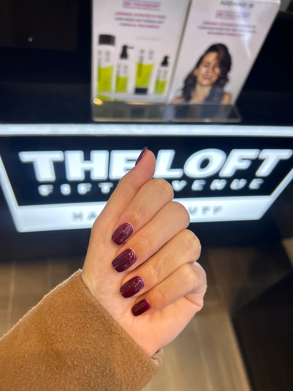 Glossy plum manicure photographed in front of the illuminated The Loft sign