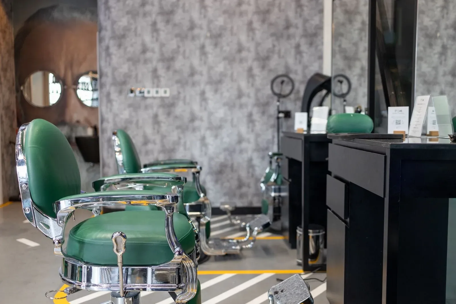 Row of vintage green leather barber chairs against a textured grey wall