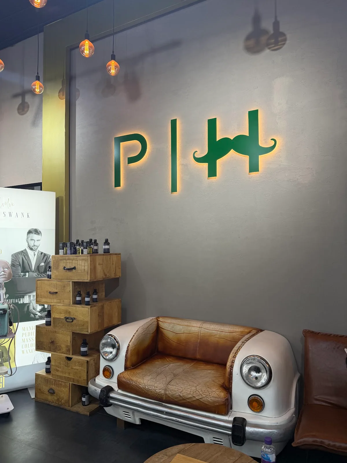 Backlit green P H logo on the wall above a car-front leather sofa