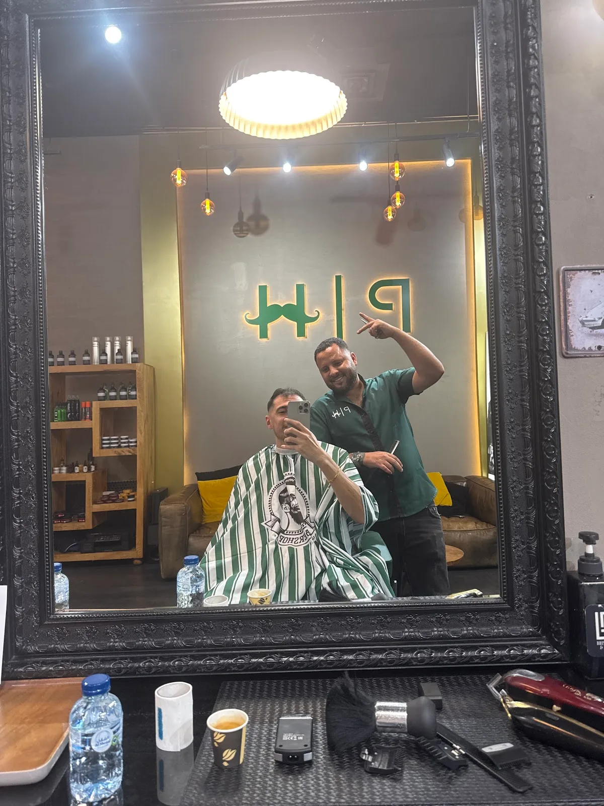 Client in a green striped barber cape getting a cut, seen in the framed mirror