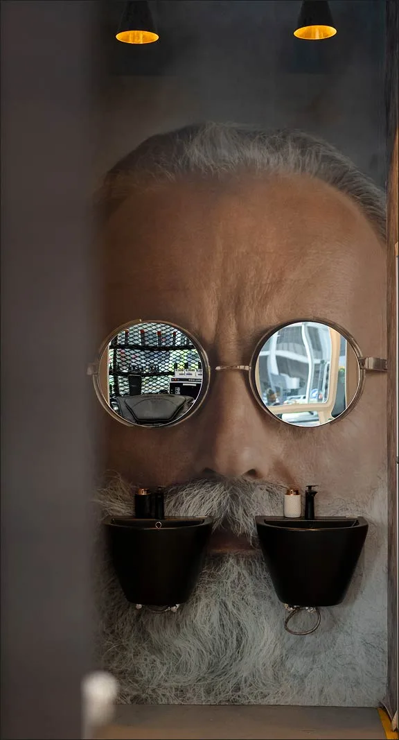 Signature wall at Project Hairway: a giant grooming-themed face mural with round mirrors for glasses and black basins