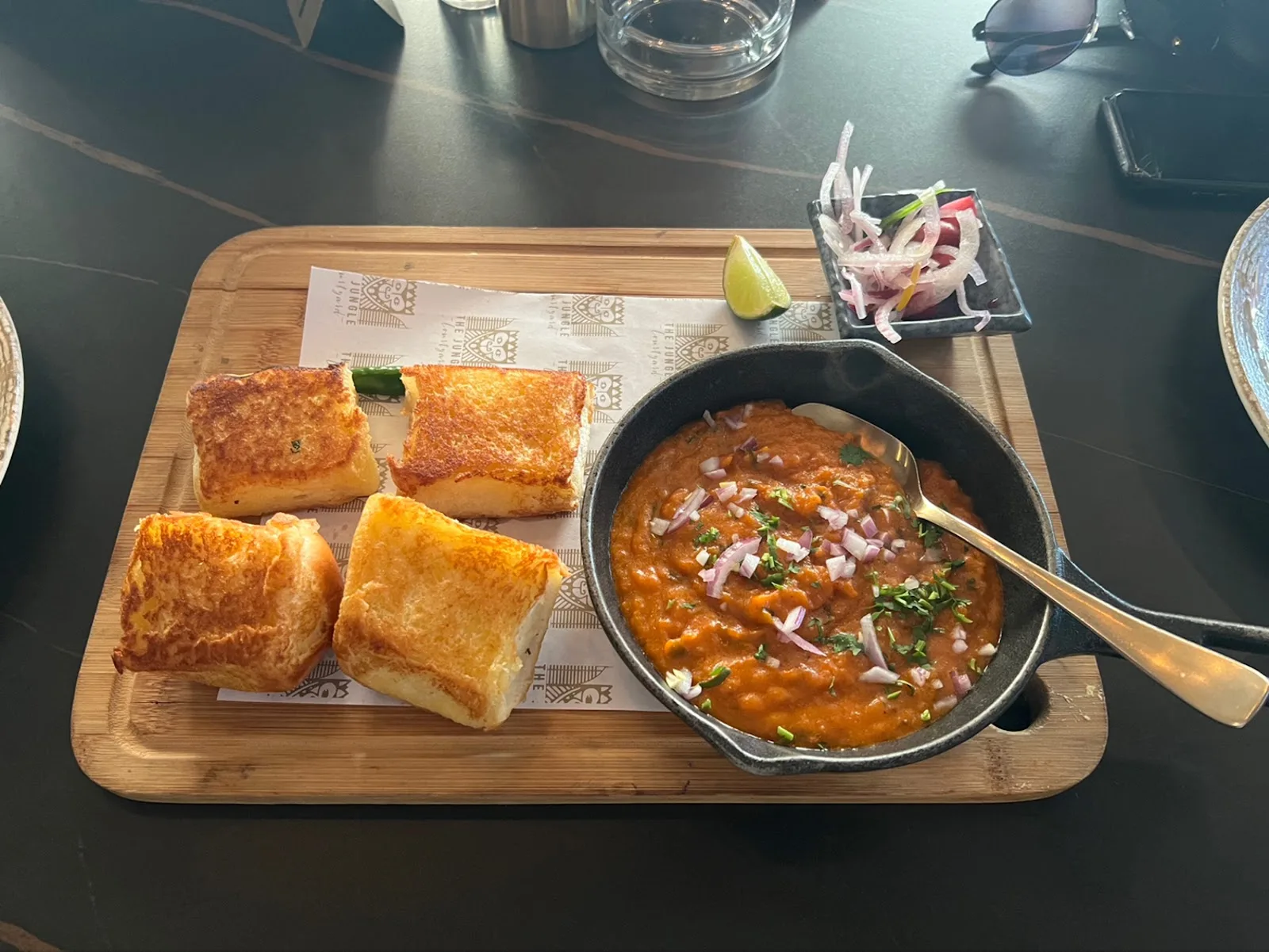 Pav bhaji — a skillet of spiced mashed vegetable curry topped with onions, with buttered toasted buns