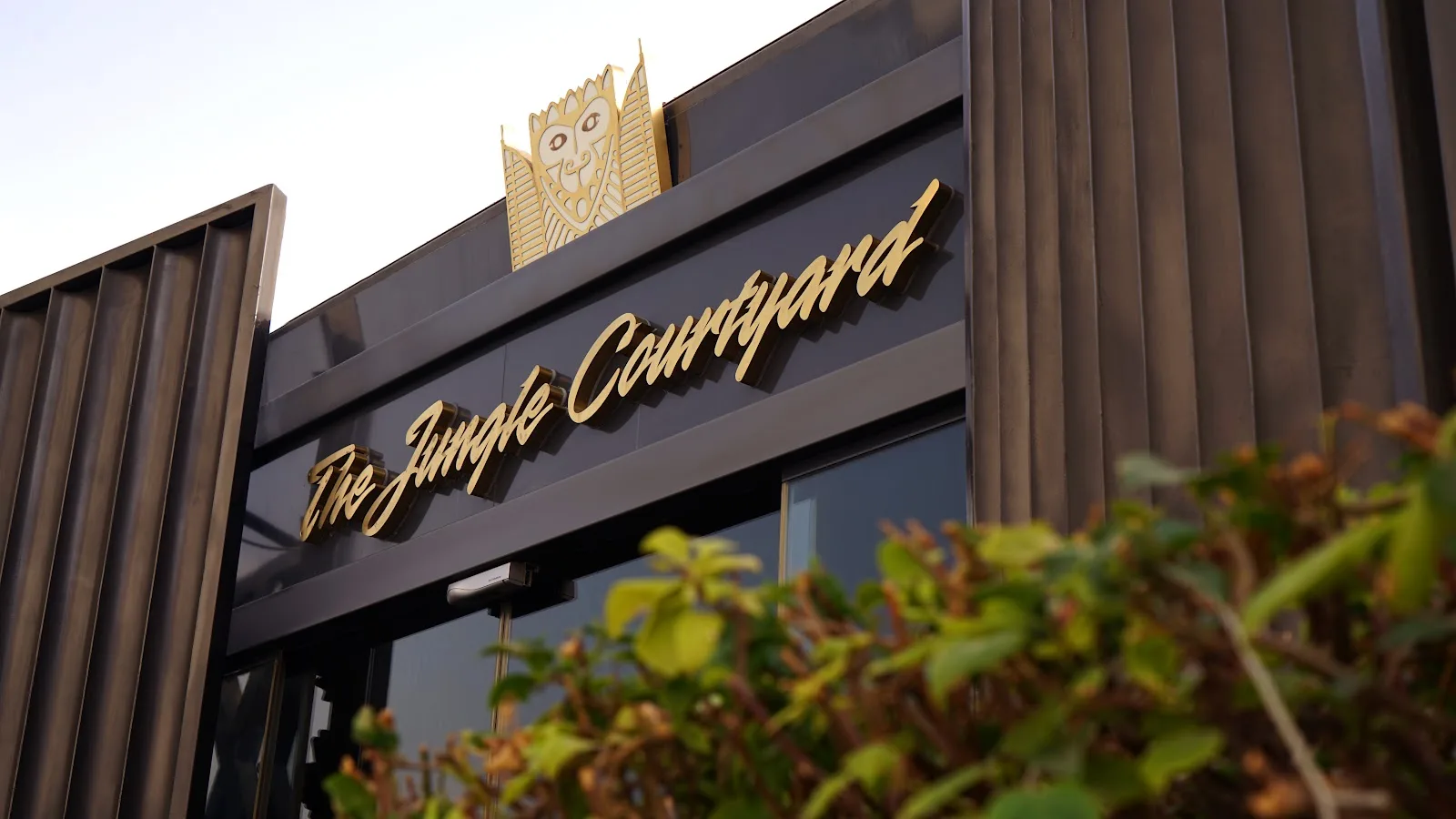 Close-up of the gold script 'The Jungle Courtyard' sign on the dark canopy, framed by greenery