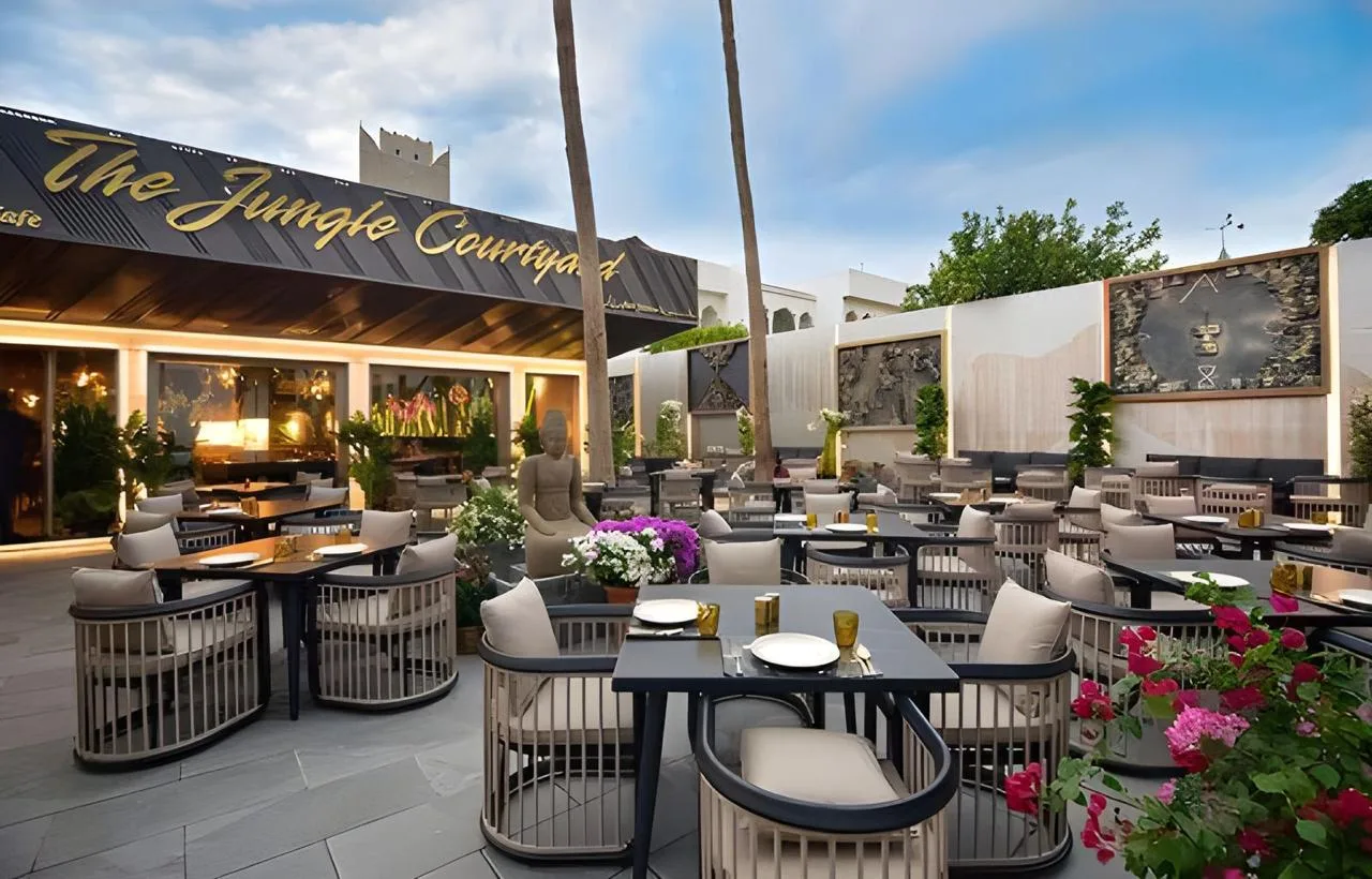 The full garden courtyard at dusk with tables, palms and flowering plants under the entrance sign
