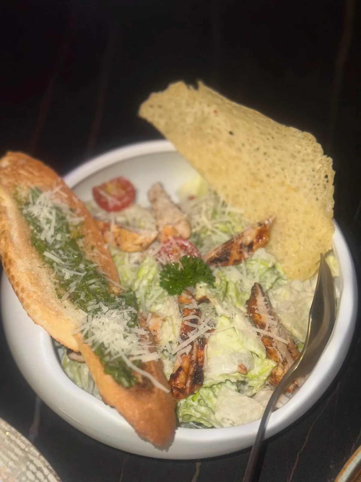 A Caesar salad bowl with grilled chicken, parmesan crisp and a pesto crostini