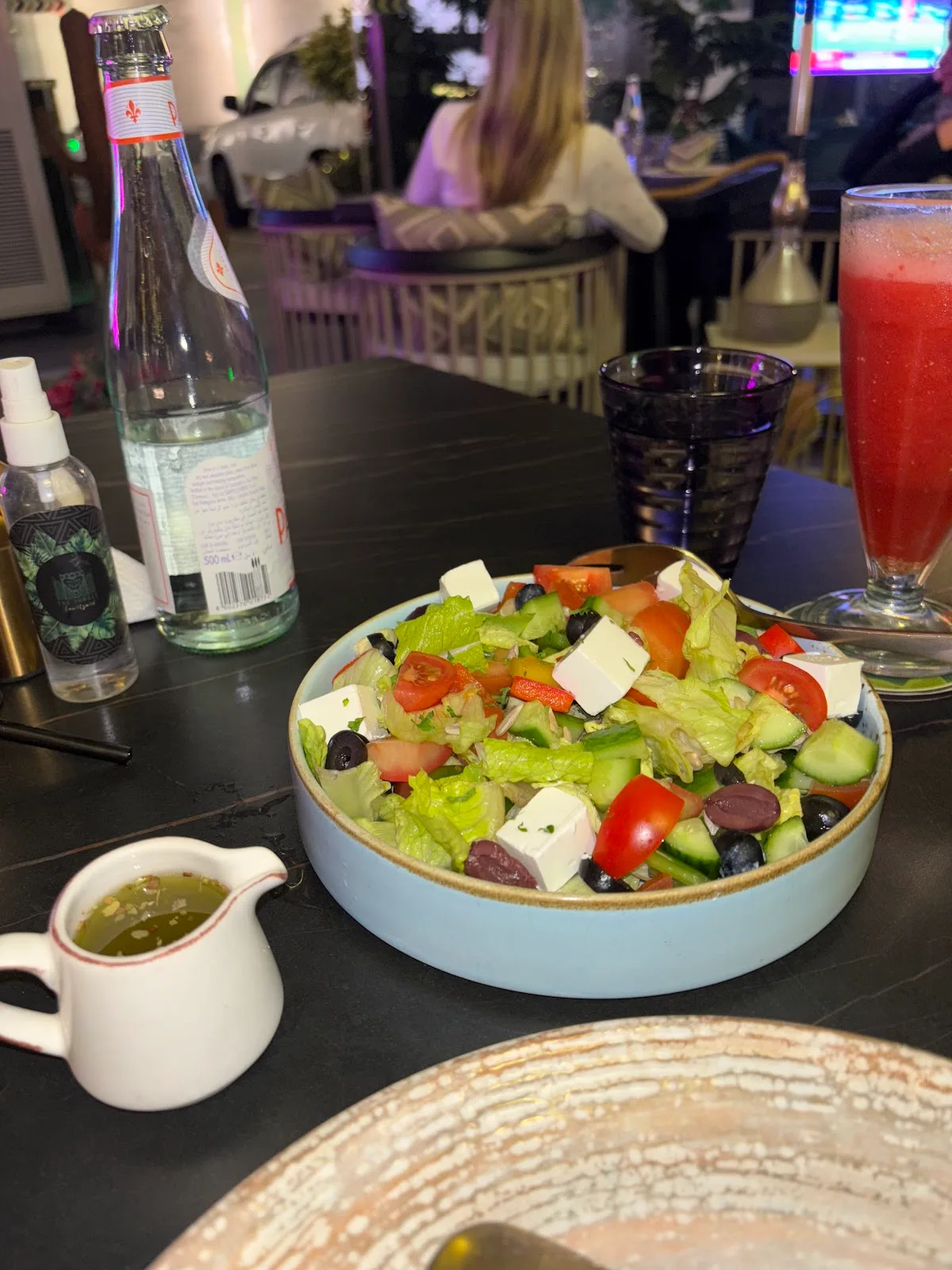 A fresh Greek-style salad with feta, olives, tomato and cucumber in a blue bowl with a jug of dressing