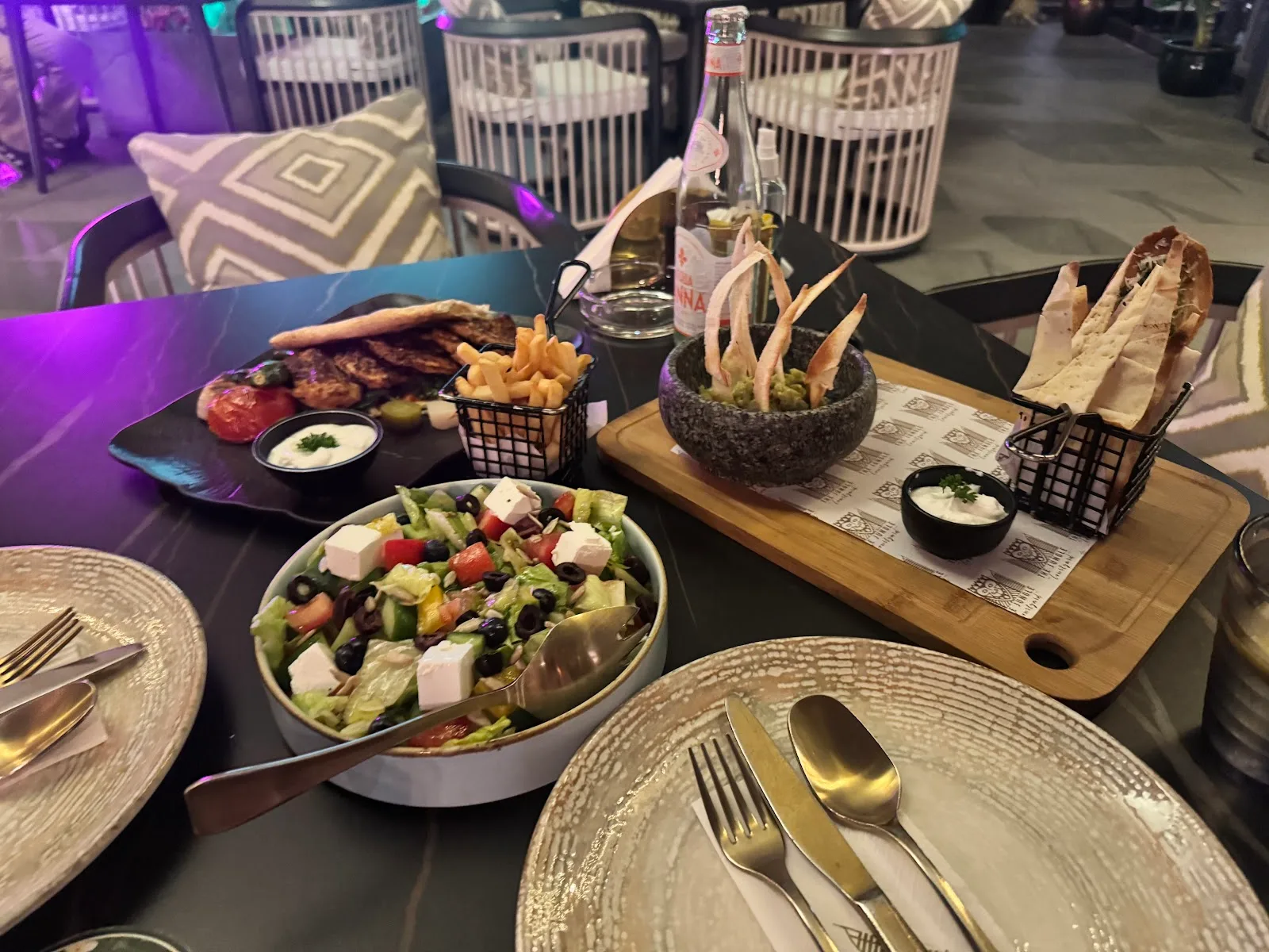 A table laid with salad, guacamole with crisp breads and gold cutlery under purple lounge lighting