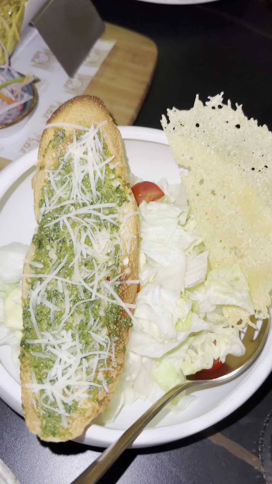 Pesto garlic bread topped with grated cheese served with a side of crisp salad leaves