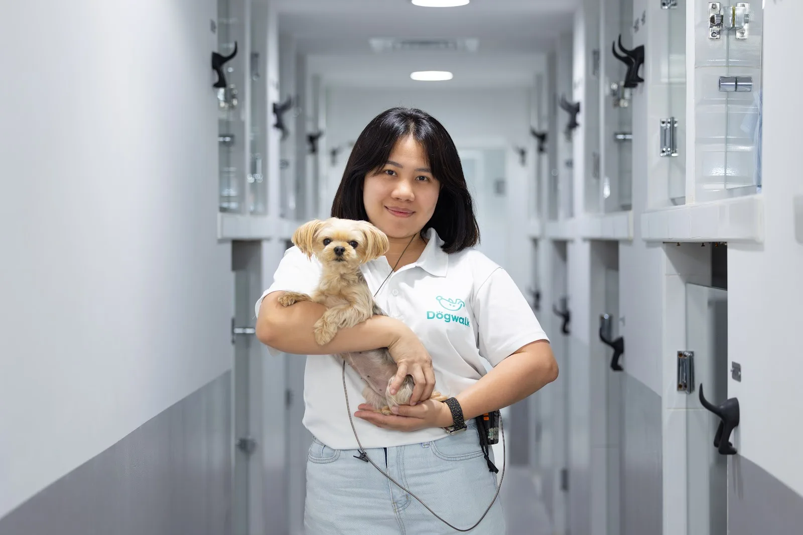 A Dogwalk team member carrying a small dog along the boarding suites