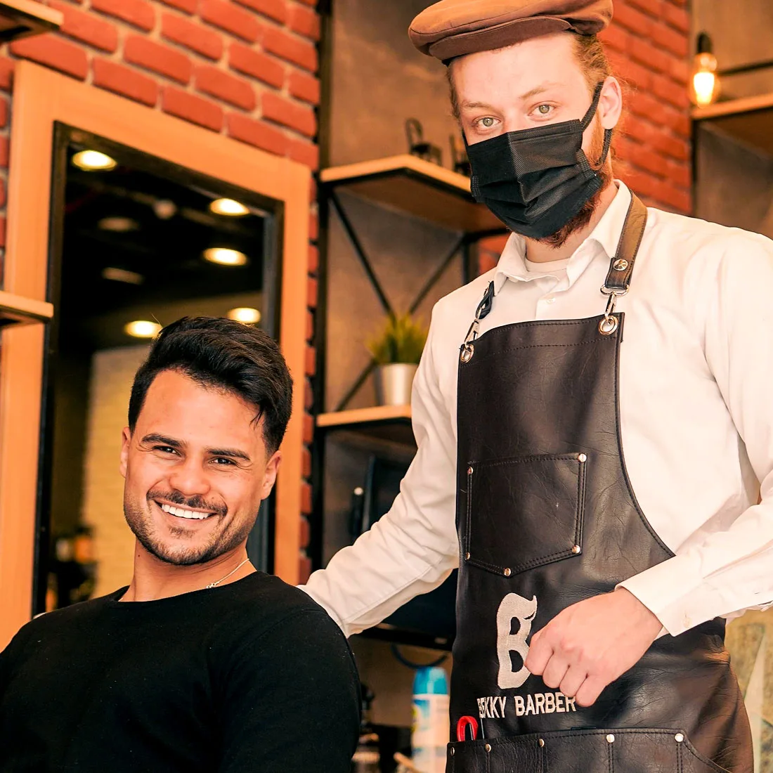Barber in apron standing beside a smiling client