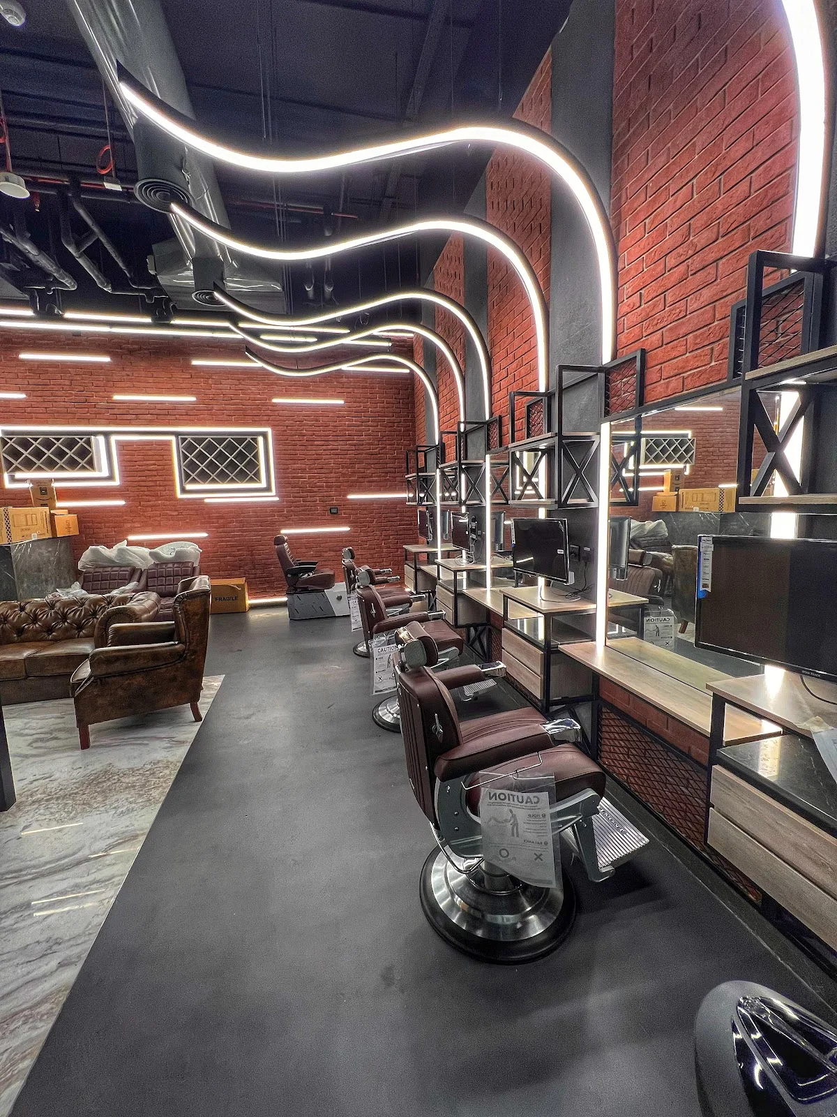 Row of barber chairs along an exposed brick wall with wave lighting