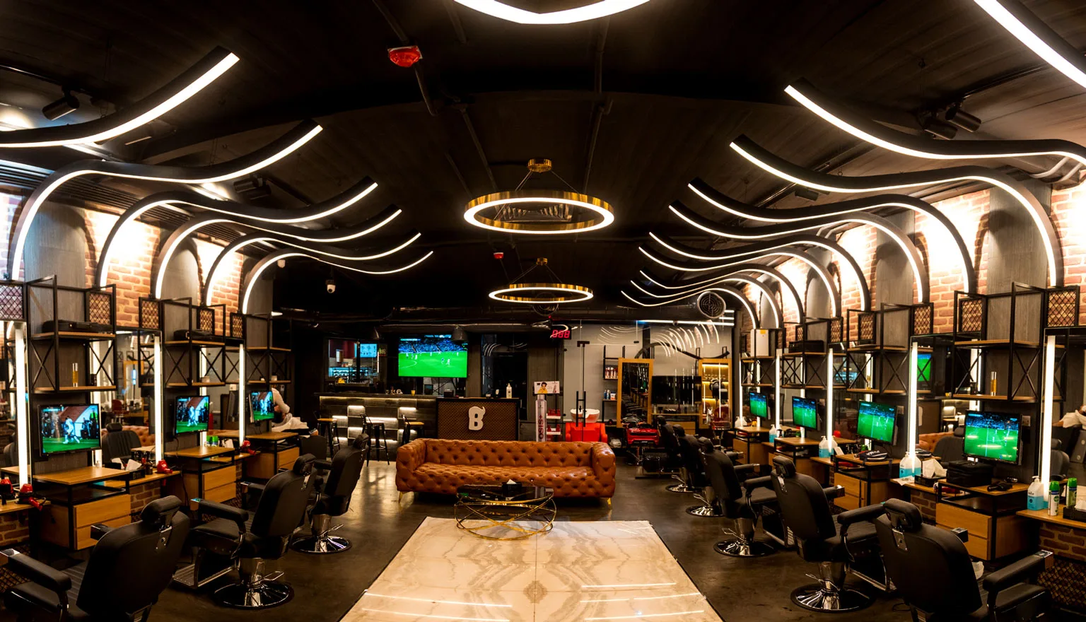 Interior of Bekky Barber Beachfront — barber chairs beneath sweeping neon ceiling lights and exposed brick