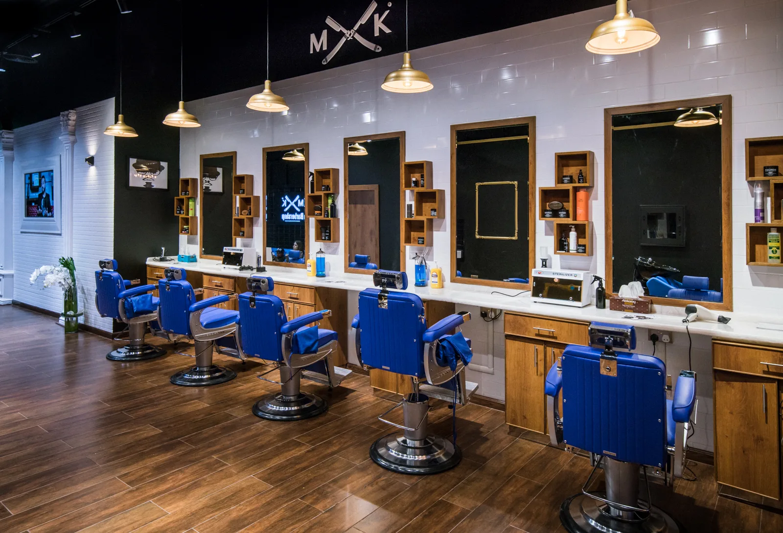 MK Barbershop interior — a row of royal-blue barber chairs under brass pendant lights