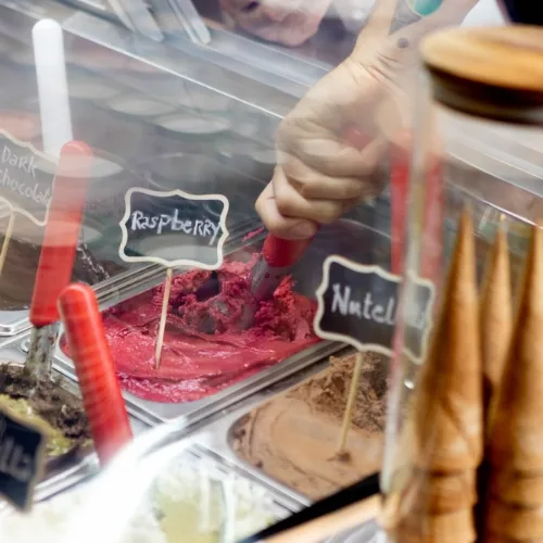 Display case of gelato with hand-written flavour labels including Raspberry and Nutella