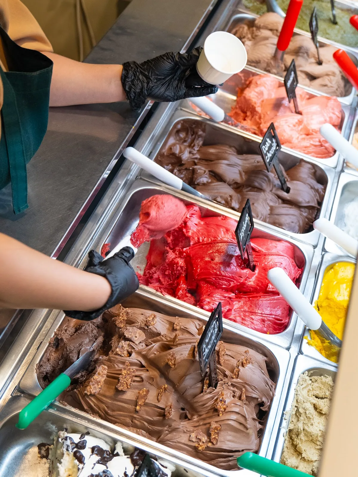 Staff scooping gelato from the rotating trays in the display case