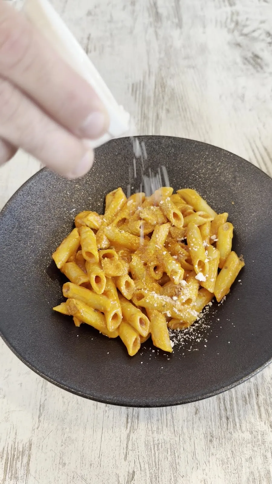 A bowl of penne pasta finished with grated cheese