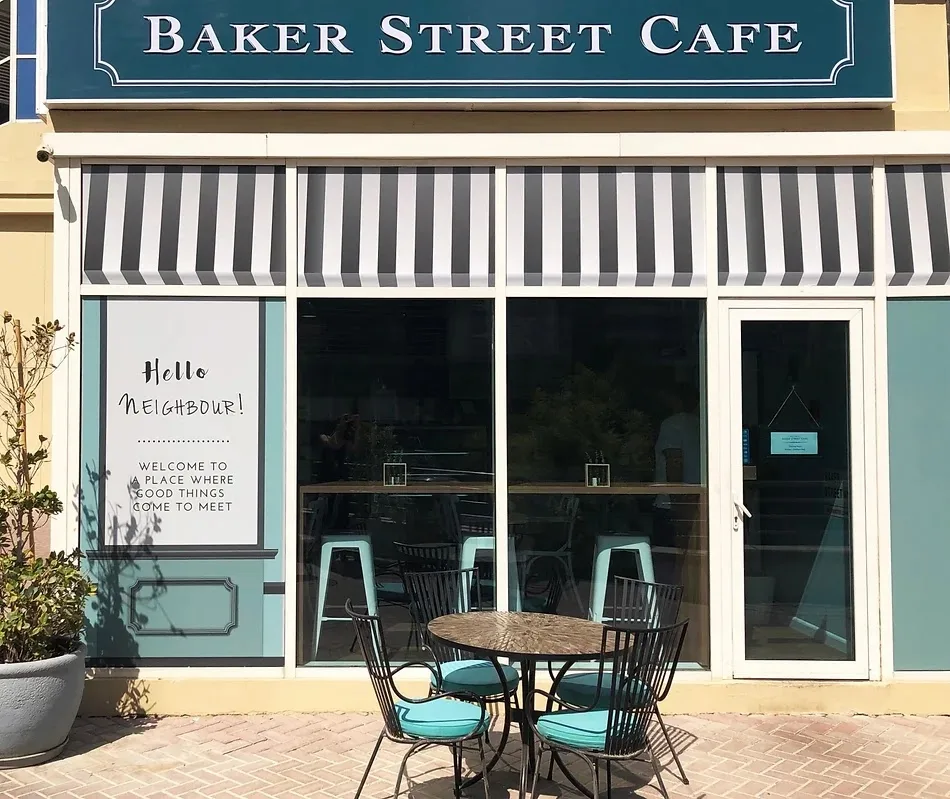 Baker Street Cafe storefront with a teal sign, striped awning and outdoor seating