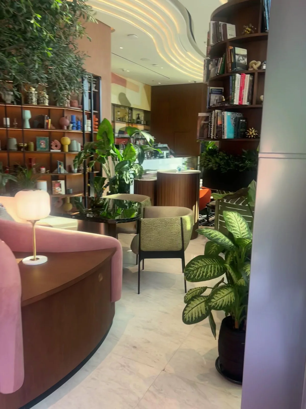 Pink velvet reading nook lined with bookshelves and plants