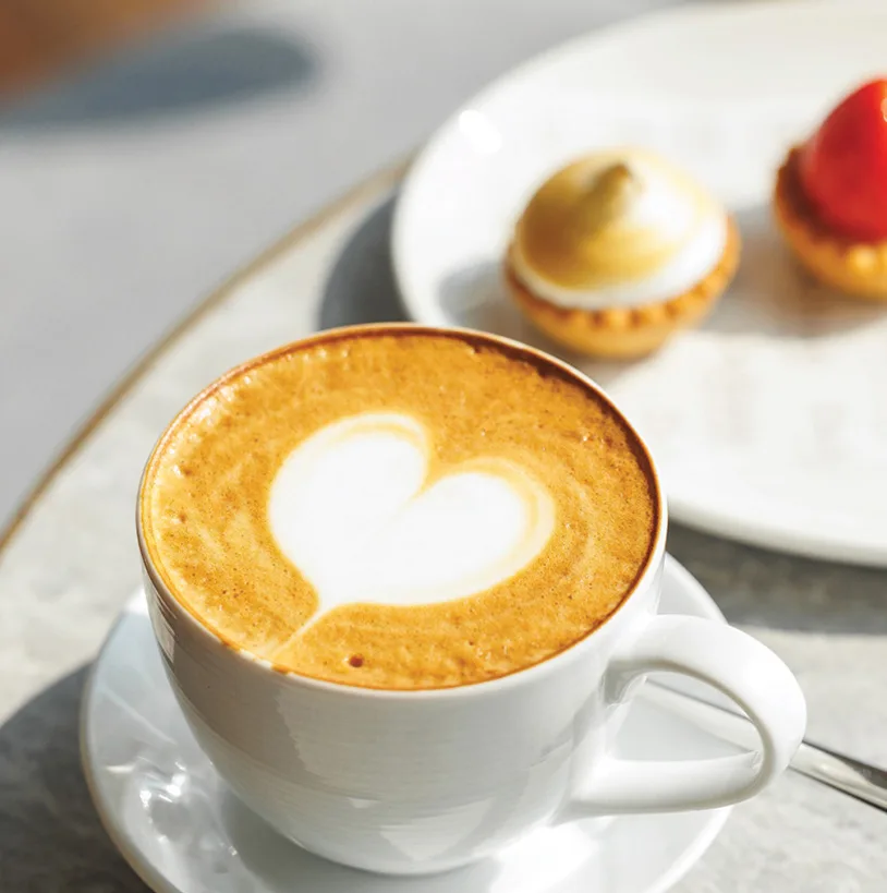Cappuccino with heart latte art beside mini tarts