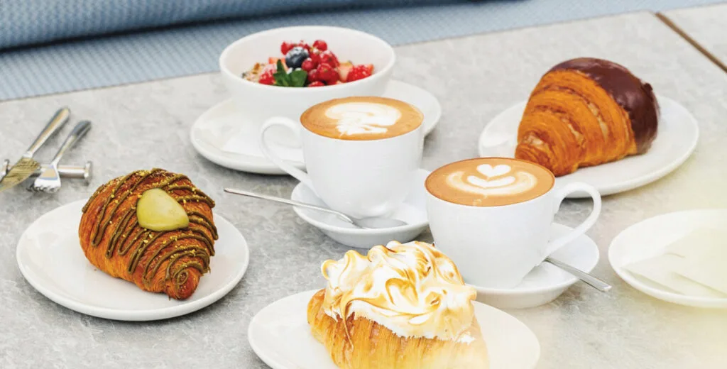 Breakfast spread of croissants, cappuccinos and a berry bowl