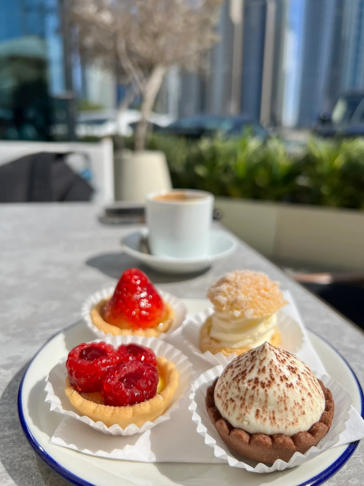 A plate of mini tarts and pastries with espresso and a marina view