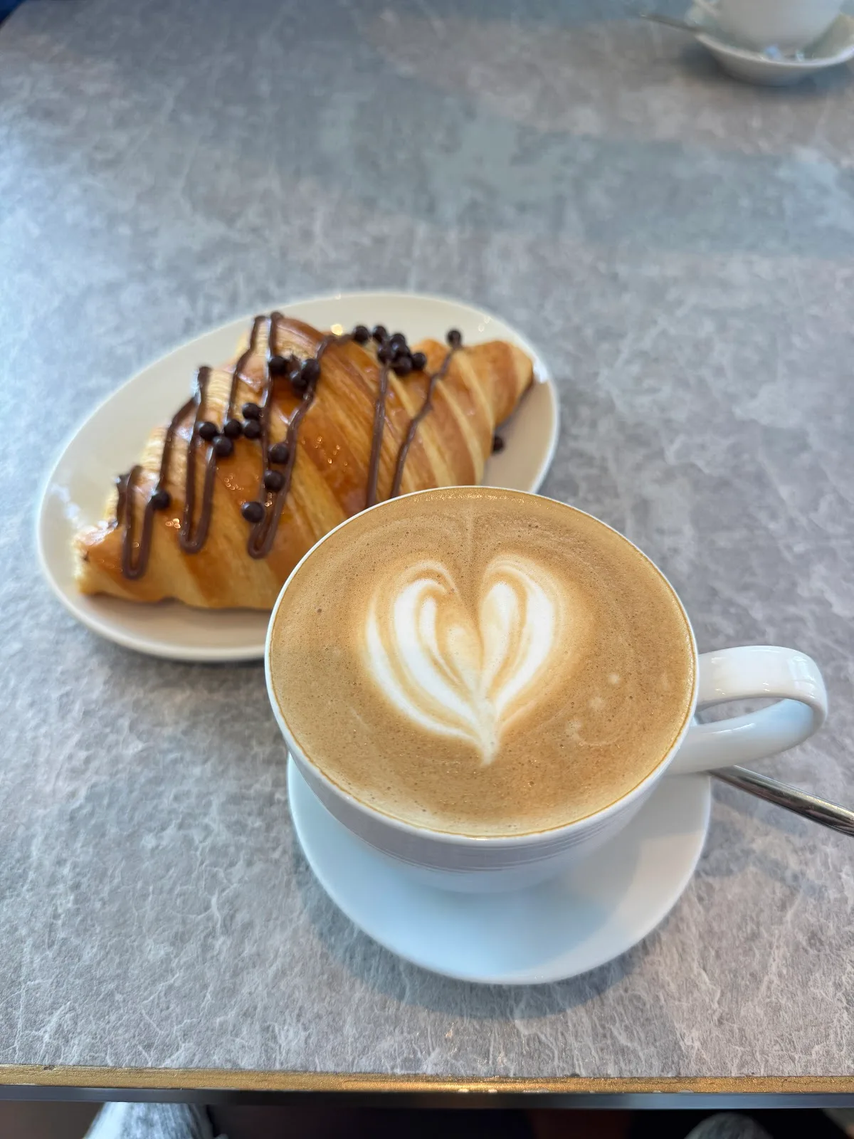 Cappuccino with latte art beside a chocolate-drizzled croissant