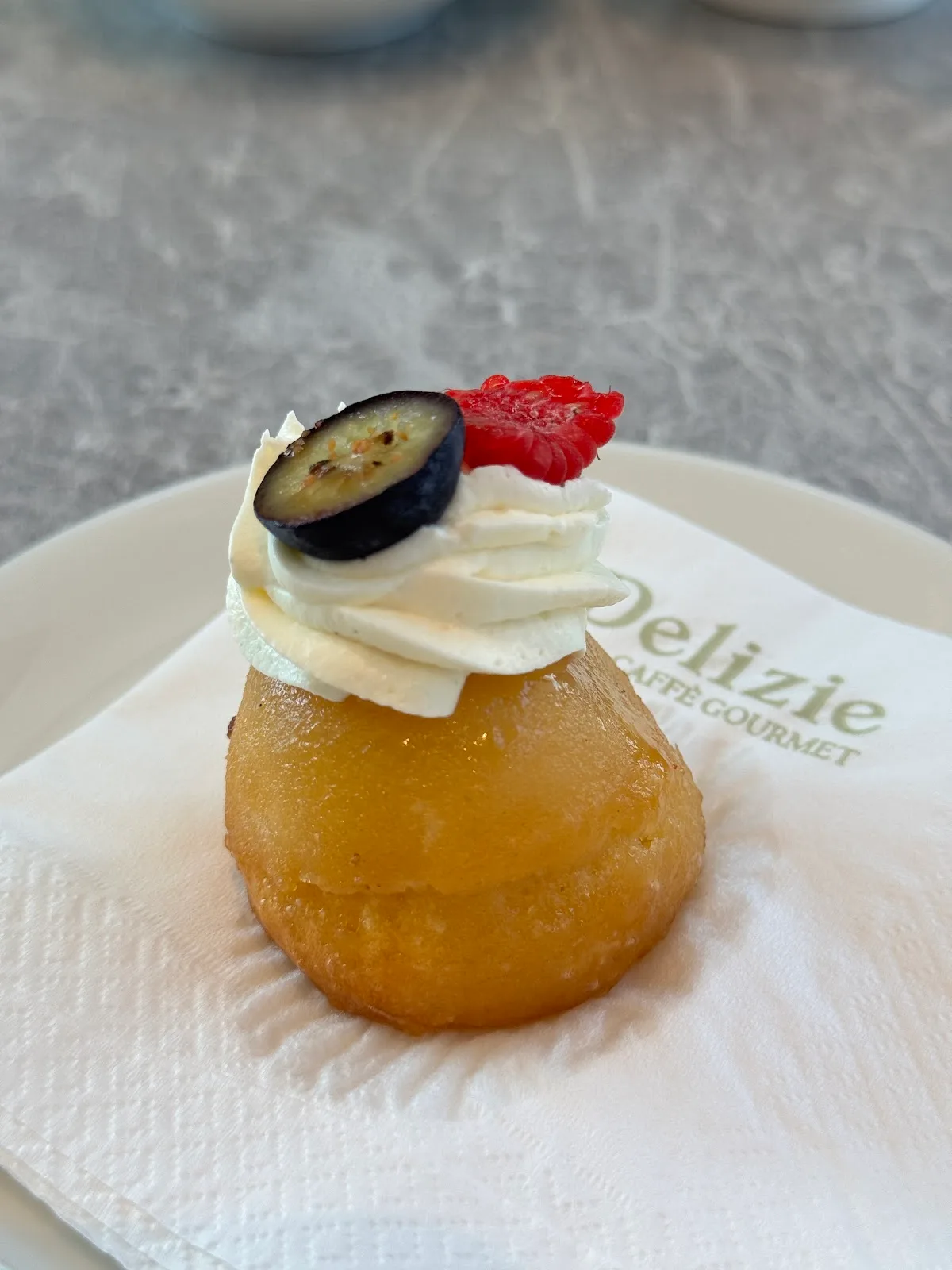 A rum baba topped with cream and berries on a Delizie napkin