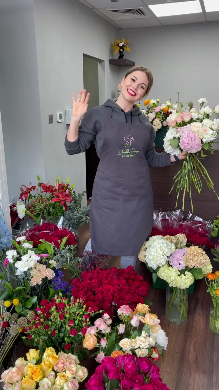 A Double Jenya florist smiling among buckets of fresh roses, carnations and hydrangea in the studio