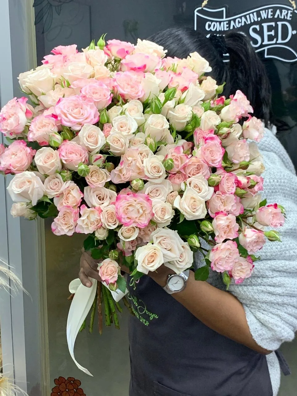 A Double Jenya florist holding a large bouquet of blush and cream spray roses at the shopfront