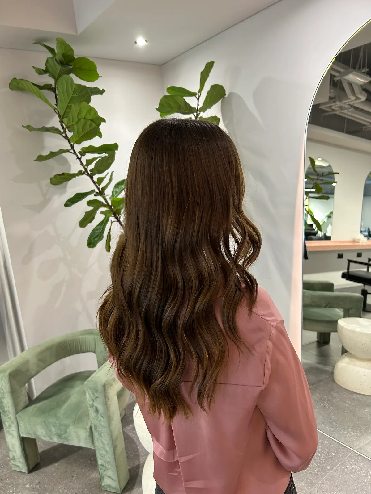 A client at Unik Hair Studio with long, glossy waved brunette hair beside an arched mirror