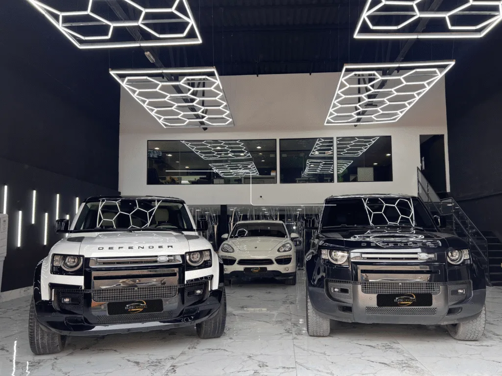 Two Land Rover Defenders and a Porsche inside Elite Crystal Car Care's Dubai studio under hexagon LED lighting