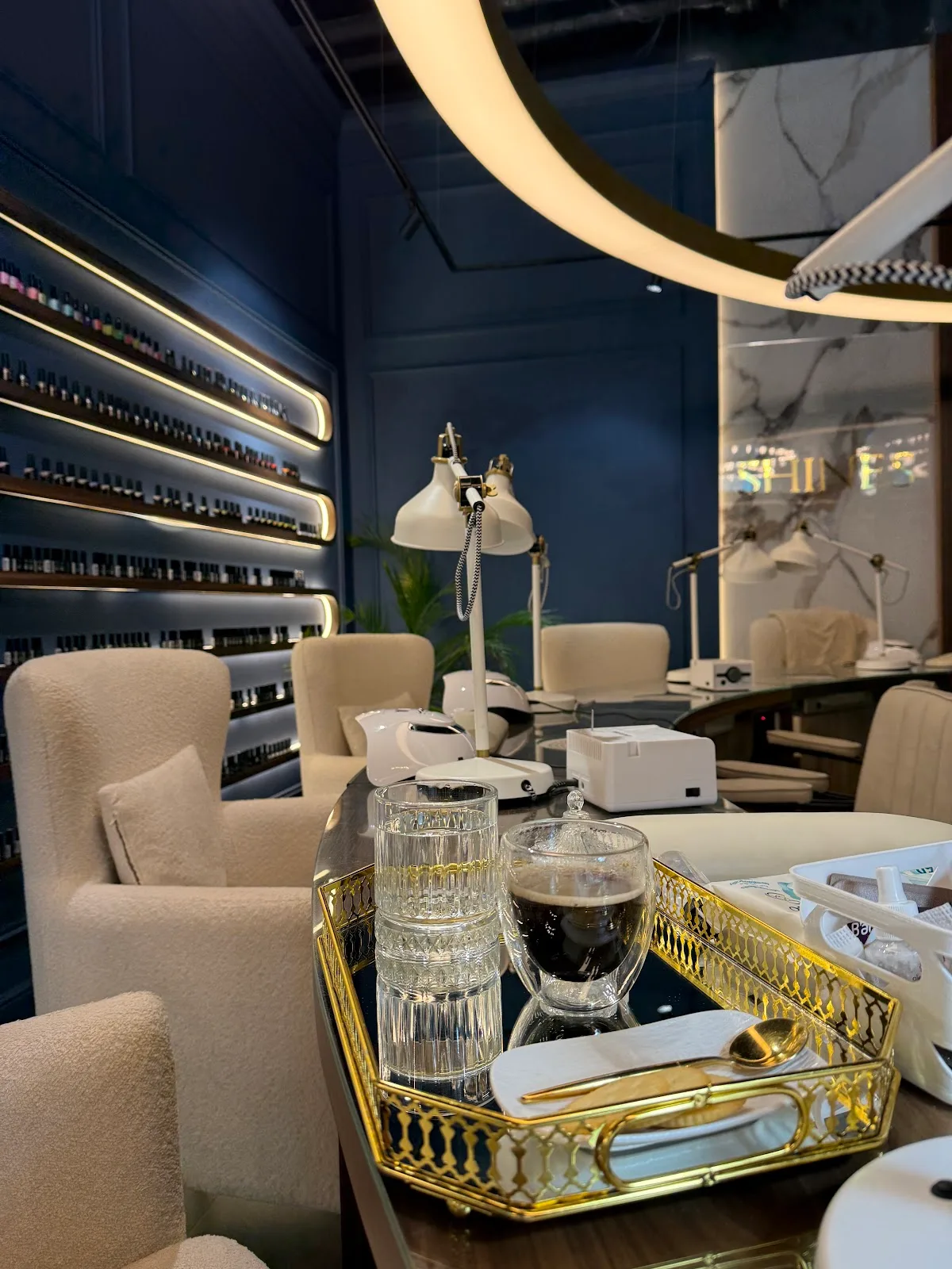 Shines salon interior — navy polish wall with gold lighting and boucle chairs