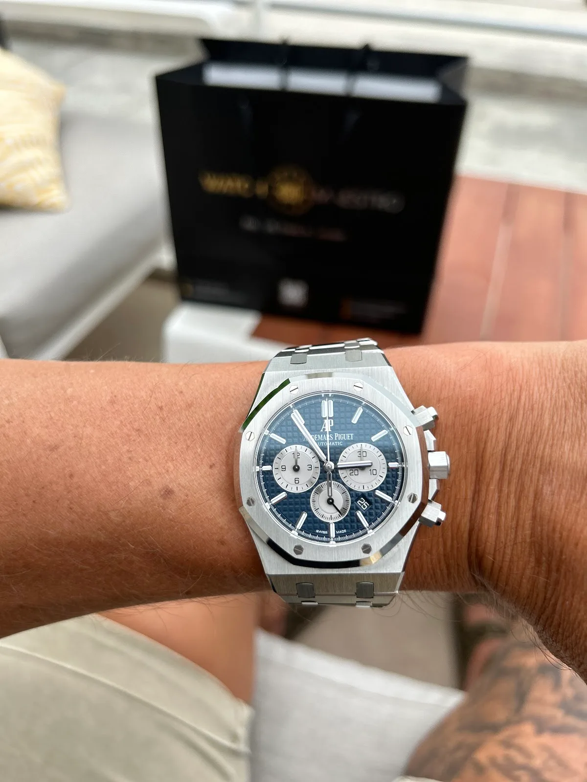 Steel Audemars Piguet Royal Oak chronograph with blue dial worn on the wrist beside a WatchMaestro bag